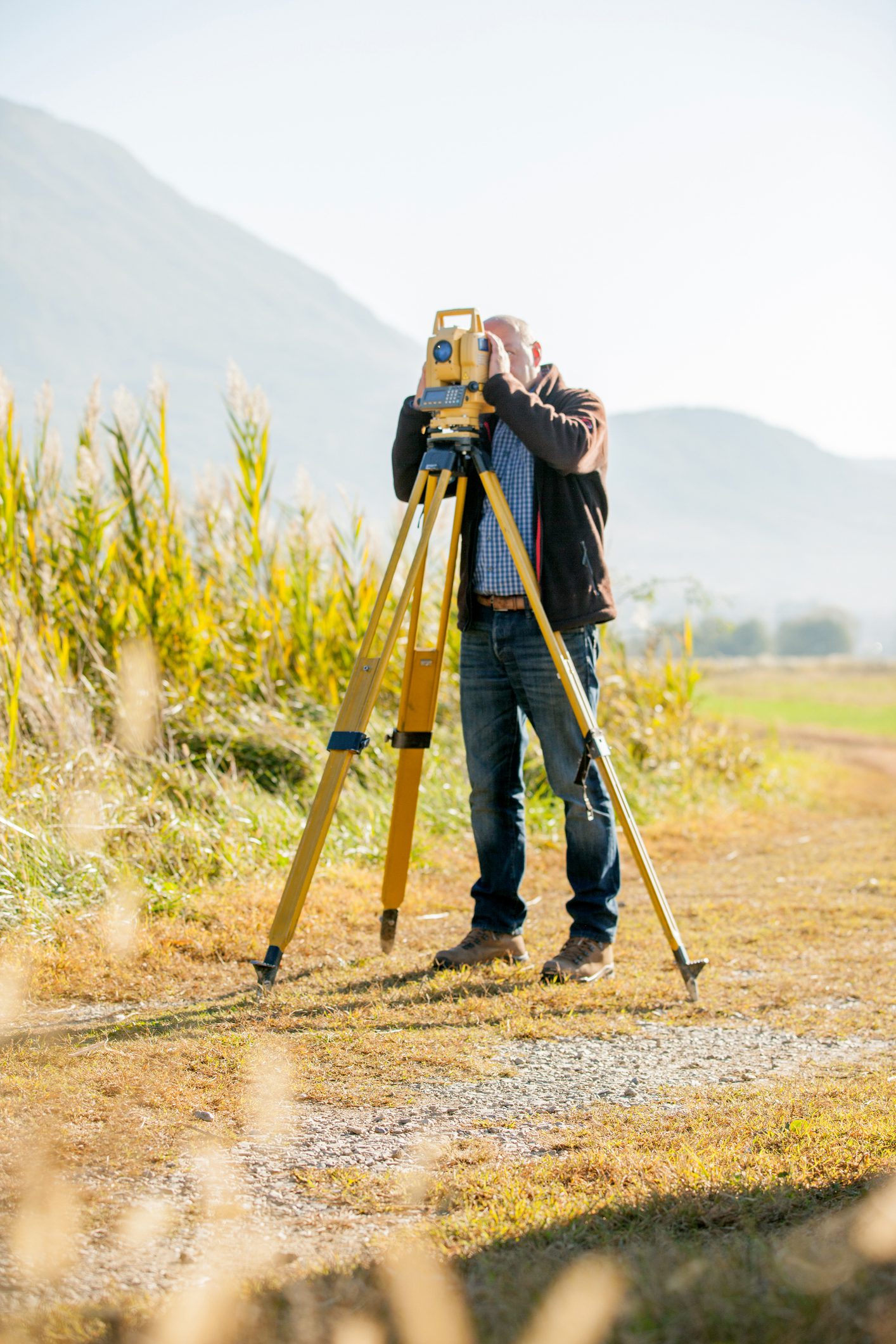 Male Surveyor Looking Thorugh Theodolite in Rural Scene.